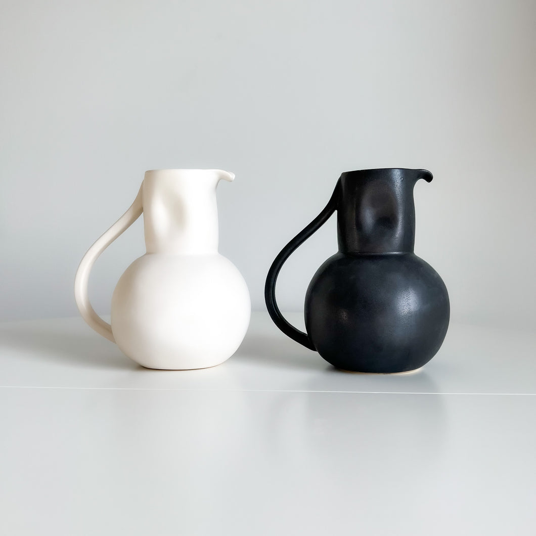 white and black pitcher with a handle sitting on a white shelf