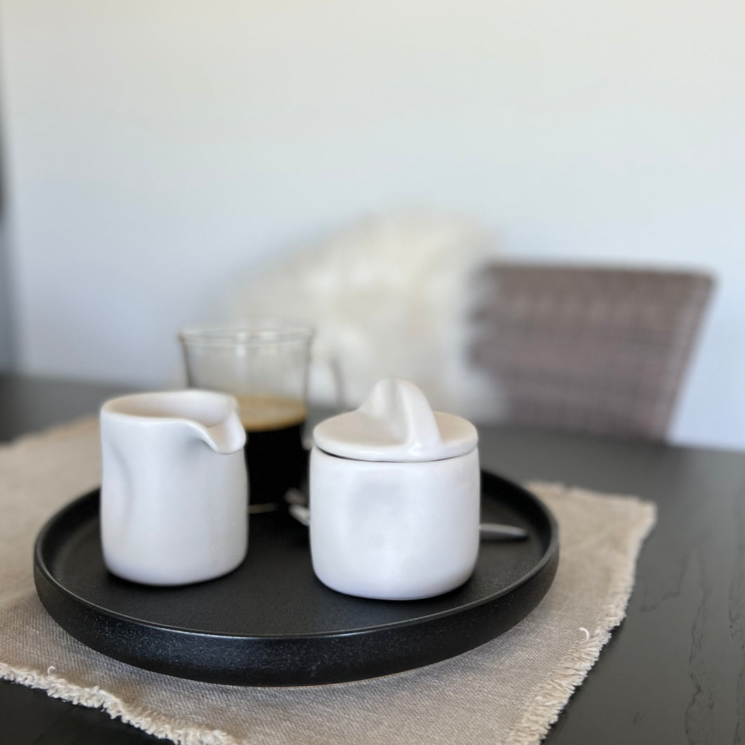 White creamer cup and bowl with lid on a black plate